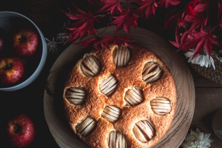Torta di mele della mia infanzia e tutto quello che ho imparato dopo aver smesso di succhiare il leccapentole. Sono al mio terzo giorno di sveglia all'alba, una pratica che si sta rivelando utile come mai avrei immaginato. Ne percepivo la potenza, mentre cercavo di familiarizzare con questo progetto di ristrutturazione della mia quotidianità durante il periodo natalizio, ma solo mettendolo in pratica riesco a capirne concretamente la portata. Scrivere queste righe però so mi costerà una gran fatica. Non tanto per il sonno, che non avverto affatto, quanto per le immagini che inevitabilmente evocherò ricordando le pagine dei libri che hanno fatto la mia storia di vita: ricordi di cene in compagnia, pranzi primaverili all'aria aperta, infornate notturne e viaggi gourmand in cui il cibo ed il vino sono stati protagonisti assoluti. Un reportage di ricordi che può affaticare parecchio chi ha scelto di affrontare un periodo detox a base di frullati Sirt. Sono consapevole che il 90% di voi non abbia idea di cosa io stia parlando, eppure è curioso sia stato proprio uno dei miei più affezionati amici social (altrimenti detti follower) a mettermi questa pulce nell'orecchio - la dieta Sirt - che ora non riesco più a ignorare. Ricapitolando: inizio questo 2020 rimuovendo l'applicazione di whatsapp, infilandomi sotto le coperte alle 21.30 e svegliandomi alle 5.30 in una stagione in cui pure il pavimento in legno risulta freddo come il ghiaccio. A questo segue saluto all'alba con 30 minuti di intensa attività fisica e un regime alimentare di "pulizia" del corpo che mi accompagna per la giornata intera e che si basa sull'assunzione di estratti di cavolo riccio, sedano, te matcha, cipolle rosse, rucola, limone, noci, zenzero e peperoncino. L'unica gratificazione, che mi trattiene dal trasformarmi nell'esorcista, sono 20 g di cioccolato fondente Lindt Excellence 85% che assaporo - come fosse acqua nel deserto - con il caffè delle 14 (perchè se scrivo"dopo pranzo" iniziereste davvero a dubitare della mia salute mentale). Sono convinta che esista qualche probabilità che io riesca a sovvertire usi e costumi che hanno governato i miei primi 40 anni di vita, tuttavia credo più probabile che entro fine settimana verrò colta da una crisi d'identità. Perchè certo, io posso anche evitare di bere aperitivi ed alimentarmi con pasta e dolci, ma non posso esimermi dal frequentare la cucina per infornare o studiare libri di ricette. Altrimenti cosa mi alzo alle 5.30 a fare? Tuttavia, impastare pane e dolci con una bibita fredda che sa di erba sul tavolo è davvero sfidante. Bene, e ora che le presentazioni sono fatte e io mi sono riempita la bocca con tutte le noci concesse per la giornata, possiamo passare a rivangare ricordi zuccherosi. Il Blitz di mele soffice con latte e rum è stato il dolce di casa negli anni in cui era un'emozione vedere mamma impastare la pizza Catarì, guardare Cinema in famiglia il venerdì sera tutti insieme su uno stesso divano e ascoltare dischi ballando selvaggiamente in salotto con mia sorella. La mia Ninetta (così la chiamo) è sempre stata metodica e precisa: in qualsiasi attività domestica, così come in cucina, non ci faceva intervenire un granchè, ma le piaceva tenere la nostra attenzione puntata sulla preparazione concedendoci qualche pezzetto di mela, delle noci, del cioccolato o la spatola ancora velata di impasto subito dopo aver infornato la torta. A me il cucchiaio, a Laura la terrina gialla o viceversa. Ricordo simpaticamente le prime sniffate di vanillina e il profumo potente della fialetta di Rum, il rumore assordante dello sbattitore che prima era stato di mia nonna (quando gli elettrodomestici duravano anche più di 20 anni) e la polvere impercettibile sospesa nell'aria quando passava a setacciare farina e lievito. Non dava il giro a 30 ricette, ma si giostrava principalmente con quelle 3 o 4 che le garantivano una standing ovation: la torta allo yogurt (in cui l'unica unità di misura era il vasetto), la torta di mele, noci e caramello e il Blitz di mele soffice con latte e rum, una ricetta tedesca che credo sia apparsa in quasiasi rivista di cucina negli anni '80. Le ho ritrovate sfogliando il suo spesso ricettario in pelle lavorata che non è affatto un cimelio di guerra, nonostante mia madre sia una signora di una certà età (non vi dirò quanti per non rischiare la vita, ma vi basti sapere che mi ha avuta a 39 e io ne ho appena compiuti 40). Ebbene la mia Ninetta ha iniziato a farcire il suo spesso ed elegante raccoglitore solo una decina d'anni fa, racimolando foglietti, ritagli di giornale e appunti che custodiva non so dove, ed è riuscita a renderlo romantico come solo un album di foto di famiglia in bianco e nero può essere. Lo conserva insieme ad altri libri di cucina sullo scaffale di una libreria bianca che delimita la sua cucina, accanto alle foto di due bimbe con le lunghe trecce e gli occhi vispi. La stessa abitudine a tenere a portata di mano preziosi ricordi l'ho fatta mia quando sono andata a vivere da sola, nel lontano 2008. Foto e libri a me cari erano stati caricati sulle mensole Ikea con le quali avevo arredato una grande parete della mia prima cucina, all'età di 26 anni. Ogni tanto, la sogno ancora. Era enorme, luminosa e dalla finestra accanto al lavello potevo vedere le Dolomiti. Avevo fatto tutto da sola: rilevazione delle misure, progetto, scelta delle finiture, disposizione degli elettrodomestici. Ci lavoravo con costanza nei fine settimana e facevo di tutto per far quadrare quei tanti moduli in un piccolo budget. Per quanto semplificassi, su una cosa sapevo di non voler scendere a compromessi: doveva essere laccata bianca con il top in legno di betulla. Dovetti sembrare talmente orgogliosa dei miei 6 fogli di progetto che, quando mi recai in negozio per la conferma d'ordine, la ragazza del reparto quasi si commosse. Ricordo ancora quel giorno con una lucidità unica: lei prima misurò con il righello ogni modulo sulla pianta, poi caricò l'ordine e infine mi confermò l'importo pari a 4,950 euro. Brava Ciètta, mi dissi, per un pelo ci sei stata dentro. Poi mi guardò attraverso i suoi occhiali blu e aggiunse: "senti, voglio farti un regalo. Ho un buono sconto del 50%, del quale sono stata omaggiata in quanto dipendente, che potrei regalare ad un amico o un parente. Se lo vuoi, è tuo."  Eh già, ho pensato anche io quello che state pensando voi... scommetto che inizia con la c. Da quella volta ebbi la certezza che la fortuna aiuta gli audaci. Sono passati 12 anni, ma quella cucina bianca e betulla con il lavello in ceramica ancora non riesco a dimenticarla. Era talmente bella che, nonostante qualche segno di evidente usura, riuscii pure a venderla prima di trasferirmi nella nuova casa con Gabriele. Quello che conservo è lo stesso modo di viverla, seppure quella attuale, più di design, funzionale e preziosa, non arrivi a regalarmi lo stesso senso di benessere. I miei libri preferiti ora in parte sono disposti su uno scaffale ricavato nella parete in rovere e, in parte, giacciono impilati su uno sgabellino accanto al bancone. Si tratta di quelli che consulto più di frequente per dissipare un dubbio, se sono in cerca di ispirazione, per un ripasso, in preda alla voglia di creare o solo come buona lettura per accompagnare un pranzo in solitaria. Nessun testo è privo di errori, ma in fondo... chi ha mai conosciuto la perfezione? Quello che spero è che in questa lista possiate scovare una porticina in grado di condurvi per le vie di qualche bel mondo ancora inesplorato. TRA I MIEI LIBRI PREFERITI DI CUCINA... Fra tagli d'Italia: dalle corna alla coda di Bruno Bassetto L'arte del menù di Fabiano Guatteri La pasticceria francese. Storie, personaggi, ingredienti, ricette di S. G. Sender e Marcel Derrien Il Pane senza impasto di Jim Lahey La grammatica dei sapori di Niki Segnit La grammatica delle spezie di Caz Hildebrand Il Montersino. Grande manuale di cucina e pasticceria di Alberto Crapari e Luca Montersino Profumo di lievito e sfoglia di Luca Montersino Best of Paul Bocuse  Non solo zucchero. Tecnica e qualità in pasticceria. Ediz. illustrata: 1 di Iginio Massari Non solo zucchero. Tecnica e qualità in pasticceria: 2 di Iginio Massari Non solo zucchero. Tecnica e qualità in pasticceria: 3 di Iginio Massari Pâtisserie, leçons en pas à pas di Philippe Urraca e Cécile Coulier (in francese) Rêves de pâtissier : 50 classiques de la pâtisserie réinventés di Pierre Hermé (in francese) La boutique delle torte. Torte, cupcakes e dolcetti da tè di Peggy Porschen The Nordic Baking Book di Magnus Nilson (in inglese) Les meilleures recettes de La Meringaie di Marie Stoclet Bardon (in francese) Pâtisserie, l'ultime référence di Christophe Felder (in francese) Jerusalem: A Cookbook di Yotam Ottolenghi (in inglese) Di farina in farina di Marianna Franchi (entrato di recente nella mia cucina! Grazie Matteo) Il pane di pasta madre di Vanessa Kimbell (entrato di recente nella mia cucina! Grazie Eleonora) Il pane è oro di Massimo Bottura Il talismano della felicità di Ada Boni RICETTA DEL BLITZ DI MELE AL LATTE E RUM Grazie mamma, per avermi trasmesso il tuo amore per le mele ed insegnato a capire l'importanza di grattugiare finemente il limone, a cogliere le sfumature delle cose, ad imparare osservando e ad intuire anche quando le verità non sono percettibili come la polvere di farina nell'aria. SUGGERIMENTI Scegliete mele non troppo grandi: affonderanno meno nell'impasto e riuscirete a disporre meglio i quarti sulla superificie. Non da ultimo, in tutte le fette ci sarà un po' di mela. Per estrarre il massimo degli olii essenziali dal limone, sfregate con i polpastrelli le zeste finemente grattugiate nello zucchero. Burro, uova e latte devono essere a temperatura ambiente. Di solito, nella preparazione dei dolci, è meglio procedere così, se non diversamente indicato. STRUMENTI sbattitore elettrico o planetaria teglia ad anello diametro circa 22 cm spatola carta forno INGREDIENTI e PROCEDIMENTO per il Blitz di mele soffice con latte e rum Per le mele 4 mele (meglio non troppo grandi) 3 cucchiai di zucchero il succo di 1 limone Per preparare il Blitz di mele soffice con latte e rum comincia lavando le mele. Sbucciale e poi dividile in 4. Rimuovi i semi, poi incidile sulla parte convessa realizzando con un coltellino affilato dei tagli paralleli e ravvicinati ma senza arrivare a inciderla del tutto. ->Per praticità, se le tue mele non sono molto grosse, puoi utilizzare il tagliauova: io pongo il quarto sulla base in plastica  e poi abbasso la leva con i fili fino ad inciderle per metà. Disponi le mele su un piatto poi bagnale con il succo di limone, spolverizzale con i 3 cucchiai di zucchero e lasciale macerare per mezz’ora. Nel frattempo, prepara l'impasto. Per l'impasto 50g +100 g zucchero semolato (tot 150 g) 70 g burro (a temperatura ambiente) 2 pizzichi di sale la polpa di una bacca di vaniglia 2 uova da allevamento a terra (a temperatura ambiente) succo e scorza di mezzo limone 200 g farina 8 g di lievito per dolci  150 g di latte intero (a temperatura ambiente) 1 cucchiaio Rum Setaccia farina e lievito assieme e tieni da parte. Imburra una teglia ad anello dal diametro di 23 cm circa e rivestila di carta forno. Separa i tuorli dagli albumi, quindi monta questi ultimi con 50 g zucchero separere gli albumi dai tuorli e montali a neve ferma. Aiutandoti con le fruste, monta il burro con i restanti 100 g di zucchero, la scorza di limone (vedi suggerimenti), la vaniglia e il sale. Quando avrai ottenuto una bella spuma, aggiungi i tuorli, uno alla volta.  Sempre montando incorpora il succo del mezzo limone. Incorpora all'impasto la farina setacciata con il lievito, alternandola con il latte cui avrai aggiunto il Rum. Porta il forno a 175° C, modalità statica. Ora lascia le fruste e prendi una spatola: incorpora all’impasto metà degli albumi montati e mescola leggermente facendo in modo che si allenti un pochino. Ora che la massa è più docile, incorpora i restanti albumi delicatamente con movimenti dal basso verso l’alto per evitare che perdano il loro volume. Per la finitura pre-cottura 2 cucchiai di olio Versa l'impasto nella teglia e disponi sopra le mele affondandole con la parte dei tagli verso l’alto. Pennellale con dell'olio, poi inforna per circa 40 minuti. Fai la prova stecchino prima di estrarla: la superficie deve risultare dorata e l'impasto non deve attaccarsi al bastoncino. Servi il Blitz di mele soffice con latte e rum tiepido e spolverizzato con dello zucchero a velo (anche un ciuffo di panna accanto ha il suo perchè).