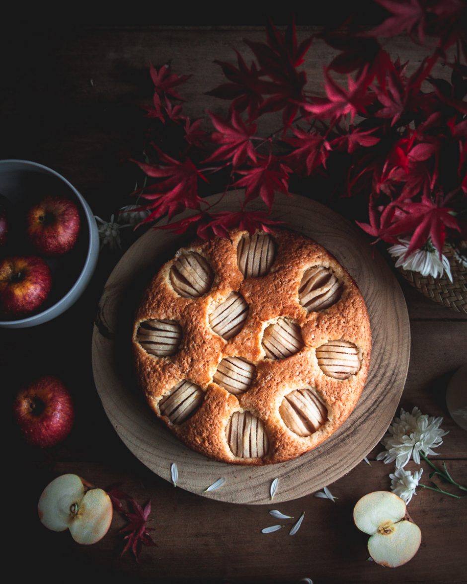 Torta di mele della mia infanzia e tutto quello che ho imparato dopo aver smesso di succhiare il leccapentole. Sono al mio terzo giorno di sveglia all'alba, una pratica che si sta rivelando utile come mai avrei immaginato. Ne percepivo la potenza, mentre cercavo di familiarizzare con questo progetto di ristrutturazione della mia quotidianità durante il periodo natalizio, ma solo mettendolo in pratica riesco a capirne concretamente la portata. Scrivere queste righe però so mi costerà una gran fatica. Non tanto per il sonno, che non avverto affatto, quanto per le immagini che inevitabilmente evocherò ricordando le pagine dei libri che hanno fatto la mia storia di vita: ricordi di cene in compagnia, pranzi primaverili all'aria aperta, infornate notturne e viaggi gourmand in cui il cibo ed il vino sono stati protagonisti assoluti. Un reportage di ricordi che può affaticare parecchio chi ha scelto di affrontare un periodo detox a base di frullati Sirt. Sono consapevole che il 90% di voi non abbia idea di cosa io stia parlando, eppure è curioso sia stato proprio uno dei miei più affezionati amici social (altrimenti detti follower) a mettermi questa pulce nell'orecchio - la dieta Sirt - che ora non riesco più a ignorare. Ricapitolando: inizio questo 2020 rimuovendo l'applicazione di whatsapp, infilandomi sotto le coperte alle 21.30 e svegliandomi alle 5.30 in una stagione in cui pure il pavimento in legno risulta freddo come il ghiaccio. A questo segue saluto all'alba con 30 minuti di intensa attività fisica e un regime alimentare di "pulizia" del corpo che mi accompagna per la giornata intera e che si basa sull'assunzione di estratti di cavolo riccio, sedano, te matcha, cipolle rosse, rucola, limone, noci, zenzero e peperoncino. L'unica gratificazione, che mi trattiene dal trasformarmi nell'esorcista, sono 20 g di cioccolato fondente Lindt Excellence 85% che assaporo - come fosse acqua nel deserto - con il caffè delle 14 (perchè se scrivo"dopo pranzo" iniziereste davvero a dubitare della mia salute mentale). Sono convinta che esista qualche probabilità che io riesca a sovvertire usi e costumi che hanno governato i miei primi 40 anni di vita, tuttavia credo più probabile che entro fine settimana verrò colta da una crisi d'identità. Perchè certo, io posso anche evitare di bere aperitivi ed alimentarmi con pasta e dolci, ma non posso esimermi dal frequentare la cucina per infornare o studiare libri di ricette. Altrimenti cosa mi alzo alle 5.30 a fare? Tuttavia, impastare pane e dolci con una bibita fredda che sa di erba sul tavolo è davvero sfidante. Bene, e ora che le presentazioni sono fatte e io mi sono riempita la bocca con tutte le noci concesse per la giornata, possiamo passare a rivangare ricordi zuccherosi. Il Blitz di mele soffice con latte e rum è stato il dolce di casa negli anni in cui era un'emozione vedere mamma impastare la pizza Catarì, guardare Cinema in famiglia il venerdì sera tutti insieme su uno stesso divano e ascoltare dischi ballando selvaggiamente in salotto con mia sorella. La mia Ninetta (così la chiamo) è sempre stata metodica e precisa: in qualsiasi attività domestica, così come in cucina, non ci faceva intervenire un granchè, ma le piaceva tenere la nostra attenzione puntata sulla preparazione concedendoci qualche pezzetto di mela, delle noci, del cioccolato o la spatola ancora velata di impasto subito dopo aver infornato la torta. A me il cucchiaio, a Laura la terrina gialla o viceversa. Ricordo simpaticamente le prime sniffate di vanillina e il profumo potente della fialetta di Rum, il rumore assordante dello sbattitore che prima era stato di mia nonna (quando gli elettrodomestici duravano anche più di 20 anni) e la polvere impercettibile sospesa nell'aria quando passava a setacciare farina e lievito. Non dava il giro a 30 ricette, ma si giostrava principalmente con quelle 3 o 4 che le garantivano una standing ovation: la torta allo yogurt (in cui l'unica unità di misura era il vasetto), la torta di mele, noci e caramello e il Blitz di mele soffice con latte e rum, una ricetta tedesca che credo sia apparsa in quasiasi rivista di cucina negli anni '80. Le ho ritrovate sfogliando il suo spesso ricettario in pelle lavorata che non è affatto un cimelio di guerra, nonostante mia madre sia una signora di una certà età (non vi dirò quanti per non rischiare la vita, ma vi basti sapere che mi ha avuta a 39 e io ne ho appena compiuti 40). Ebbene la mia Ninetta ha iniziato a farcire il suo spesso ed elegante raccoglitore solo una decina d'anni fa, racimolando foglietti, ritagli di giornale e appunti che custodiva non so dove, ed è riuscita a renderlo romantico come solo un album di foto di famiglia in bianco e nero può essere. Lo conserva insieme ad altri libri di cucina sullo scaffale di una libreria bianca che delimita la sua cucina, accanto alle foto di due bimbe con le lunghe trecce e gli occhi vispi. La stessa abitudine a tenere a portata di mano preziosi ricordi l'ho fatta mia quando sono andata a vivere da sola, nel lontano 2008. Foto e libri a me cari erano stati caricati sulle mensole Ikea con le quali avevo arredato una grande parete della mia prima cucina, all'età di 26 anni. Ogni tanto, la sogno ancora. Era enorme, luminosa e dalla finestra accanto al lavello potevo vedere le Dolomiti. Avevo fatto tutto da sola: rilevazione delle misure, progetto, scelta delle finiture, disposizione degli elettrodomestici. Ci lavoravo con costanza nei fine settimana e facevo di tutto per far quadrare quei tanti moduli in un piccolo budget. Per quanto semplificassi, su una cosa sapevo di non voler scendere a compromessi: doveva essere laccata bianca con il top in legno di betulla. Dovetti sembrare talmente orgogliosa dei miei 6 fogli di progetto che, quando mi recai in negozio per la conferma d'ordine, la ragazza del reparto quasi si commosse. Ricordo ancora quel giorno con una lucidità unica: lei prima misurò con il righello ogni modulo sulla pianta, poi caricò l'ordine e infine mi confermò l'importo pari a 4,950 euro. Brava Ciètta, mi dissi, per un pelo ci sei stata dentro. Poi mi guardò attraverso i suoi occhiali blu e aggiunse: "senti, voglio farti un regalo. Ho un buono sconto del 50%, del quale sono stata omaggiata in quanto dipendente, che potrei regalare ad un amico o un parente. Se lo vuoi, è tuo."  Eh già, ho pensato anche io quello che state pensando voi... scommetto che inizia con la c. Da quella volta ebbi la certezza che la fortuna aiuta gli audaci. Sono passati 12 anni, ma quella cucina bianca e betulla con il lavello in ceramica ancora non riesco a dimenticarla. Era talmente bella che, nonostante qualche segno di evidente usura, riuscii pure a venderla prima di trasferirmi nella nuova casa con Gabriele. Quello che conservo è lo stesso modo di viverla, seppure quella attuale, più di design, funzionale e preziosa, non arrivi a regalarmi lo stesso senso di benessere. I miei libri preferiti ora in parte sono disposti su uno scaffale ricavato nella parete in rovere e, in parte, giacciono impilati su uno sgabellino accanto al bancone. Si tratta di quelli che consulto più di frequente per dissipare un dubbio, se sono in cerca di ispirazione, per un ripasso, in preda alla voglia di creare o solo come buona lettura per accompagnare un pranzo in solitaria. Nessun testo è privo di errori, ma in fondo... chi ha mai conosciuto la perfezione? Quello che spero è che in questa lista possiate scovare una porticina in grado di condurvi per le vie di qualche bel mondo ancora inesplorato. TRA I MIEI LIBRI PREFERITI DI CUCINA... Fra tagli d'Italia: dalle corna alla coda di Bruno Bassetto L'arte del menù di Fabiano Guatteri La pasticceria francese. Storie, personaggi, ingredienti, ricette di S. G. Sender e Marcel Derrien Il Pane senza impasto di Jim Lahey La grammatica dei sapori di Niki Segnit La grammatica delle spezie di Caz Hildebrand Il Montersino. Grande manuale di cucina e pasticceria di Alberto Crapari e Luca Montersino Profumo di lievito e sfoglia di Luca Montersino Best of Paul Bocuse  Non solo zucchero. Tecnica e qualità in pasticceria. Ediz. illustrata: 1 di Iginio Massari Non solo zucchero. Tecnica e qualità in pasticceria: 2 di Iginio Massari Non solo zucchero. Tecnica e qualità in pasticceria: 3 di Iginio Massari Pâtisserie, leçons en pas à pas di Philippe Urraca e Cécile Coulier (in francese) Rêves de pâtissier : 50 classiques de la pâtisserie réinventés di Pierre Hermé (in francese) La boutique delle torte. Torte, cupcakes e dolcetti da tè di Peggy Porschen The Nordic Baking Book di Magnus Nilson (in inglese) Les meilleures recettes de La Meringaie di Marie Stoclet Bardon (in francese) Pâtisserie, l'ultime référence di Christophe Felder (in francese) Jerusalem: A Cookbook di Yotam Ottolenghi (in inglese) Di farina in farina di Marianna Franchi (entrato di recente nella mia cucina! Grazie Matteo) Il pane di pasta madre di Vanessa Kimbell (entrato di recente nella mia cucina! Grazie Eleonora) Il pane è oro di Massimo Bottura Il talismano della felicità di Ada Boni RICETTA DEL BLITZ DI MELE AL LATTE E RUM Grazie mamma, per avermi trasmesso il tuo amore per le mele ed insegnato a capire l'importanza di grattugiare finemente il limone, a cogliere le sfumature delle cose, ad imparare osservando e ad intuire anche quando le verità non sono percettibili come la polvere di farina nell'aria. SUGGERIMENTI Scegliete mele non troppo grandi: affonderanno meno nell'impasto e riuscirete a disporre meglio i quarti sulla superificie. Non da ultimo, in tutte le fette ci sarà un po' di mela. Per estrarre il massimo degli olii essenziali dal limone, sfregate con i polpastrelli le zeste finemente grattugiate nello zucchero. Burro, uova e latte devono essere a temperatura ambiente. Di solito, nella preparazione dei dolci, è meglio procedere così, se non diversamente indicato. STRUMENTI sbattitore elettrico o planetaria teglia ad anello diametro circa 22 cm spatola carta forno INGREDIENTI e PROCEDIMENTO per il Blitz di mele soffice con latte e rum Per le mele 4 mele (meglio non troppo grandi) 3 cucchiai di zucchero il succo di 1 limone Per preparare il Blitz di mele soffice con latte e rum comincia lavando le mele. Sbucciale e poi dividile in 4. Rimuovi i semi, poi incidile sulla parte convessa realizzando con un coltellino affilato dei tagli paralleli e ravvicinati ma senza arrivare a inciderla del tutto. ->Per praticità, se le tue mele non sono molto grosse, puoi utilizzare il tagliauova: io pongo il quarto sulla base in plastica  e poi abbasso la leva con i fili fino ad inciderle per metà. Disponi le mele su un piatto poi bagnale con il succo di limone, spolverizzale con i 3 cucchiai di zucchero e lasciale macerare per mezz’ora. Nel frattempo, prepara l'impasto. Per l'impasto 50g +100 g zucchero semolato (tot 150 g) 70 g burro (a temperatura ambiente) 2 pizzichi di sale la polpa di una bacca di vaniglia 2 uova da allevamento a terra (a temperatura ambiente) succo e scorza di mezzo limone 200 g farina 8 g di lievito per dolci  150 g di latte intero (a temperatura ambiente) 1 cucchiaio Rum Setaccia farina e lievito assieme e tieni da parte. Imburra una teglia ad anello dal diametro di 23 cm circa e rivestila di carta forno. Separa i tuorli dagli albumi, quindi monta questi ultimi con 50 g zucchero separere gli albumi dai tuorli e montali a neve ferma. Aiutandoti con le fruste, monta il burro con i restanti 100 g di zucchero, la scorza di limone (vedi suggerimenti), la vaniglia e il sale. Quando avrai ottenuto una bella spuma, aggiungi i tuorli, uno alla volta.  Sempre montando incorpora il succo del mezzo limone. Incorpora all'impasto la farina setacciata con il lievito, alternandola con il latte cui avrai aggiunto il Rum. Porta il forno a 175° C, modalità statica. Ora lascia le fruste e prendi una spatola: incorpora all’impasto metà degli albumi montati e mescola leggermente facendo in modo che si allenti un pochino. Ora che la massa è più docile, incorpora i restanti albumi delicatamente con movimenti dal basso verso l’alto per evitare che perdano il loro volume. Per la finitura pre-cottura 2 cucchiai di olio Versa l'impasto nella teglia e disponi sopra le mele affondandole con la parte dei tagli verso l’alto. Pennellale con dell'olio, poi inforna per circa 40 minuti. Fai la prova stecchino prima di estrarla: la superficie deve risultare dorata e l'impasto non deve attaccarsi al bastoncino. Servi il Blitz di mele soffice con latte e rum tiepido e spolverizzato con dello zucchero a velo (anche un ciuffo di panna accanto ha il suo perchè).